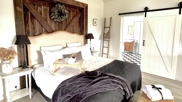 Une chambre avec un grand lit, une tête de lit en bois, une échelle, un panier en osier et un sol à carreaux.