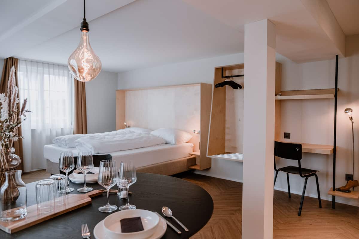 A modern hotel room with a neatly made bed, a dining table set for two, and a chair.