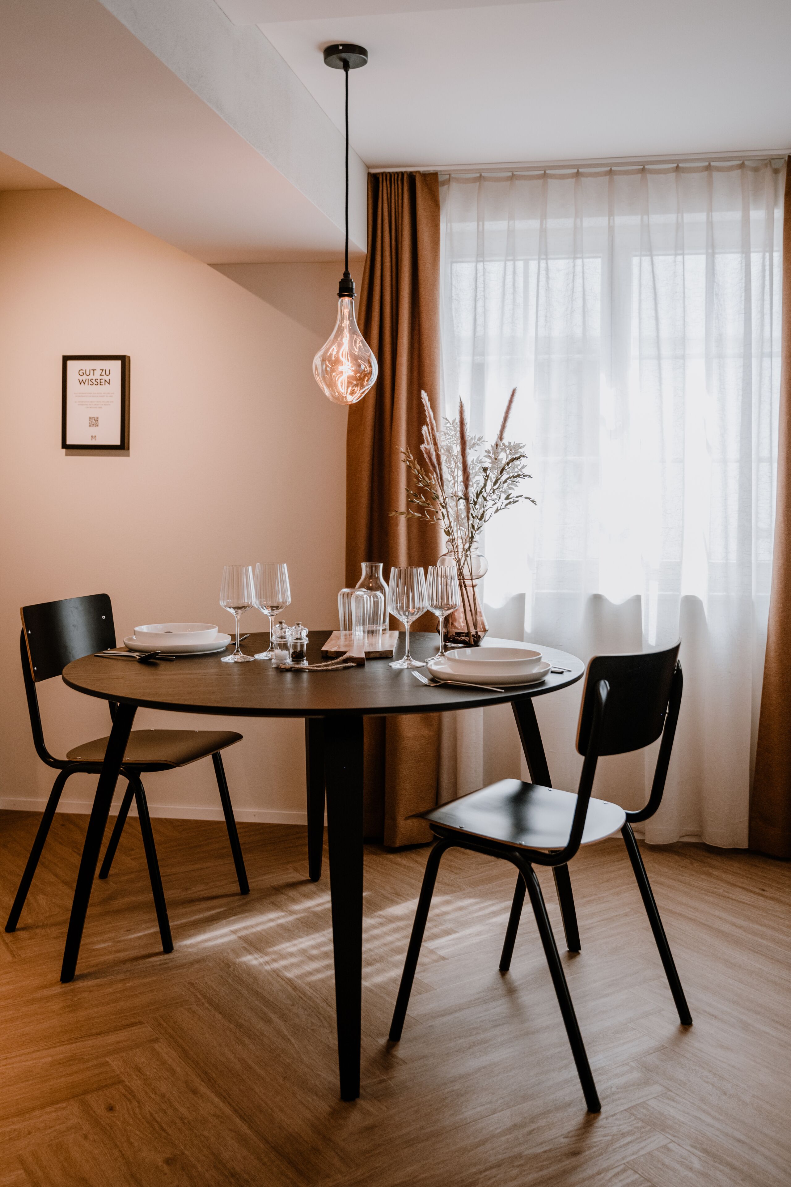A dining area with a round table, four chairs, and a hanging light fixture.