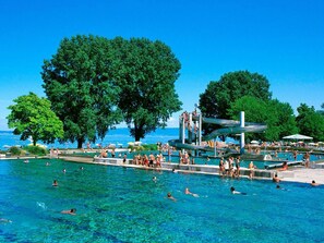 A public swimming pool with multiple lanes, surrounded by trees and a clear blue sky. - Hotel Müllers Self-Check-In (Arbon)