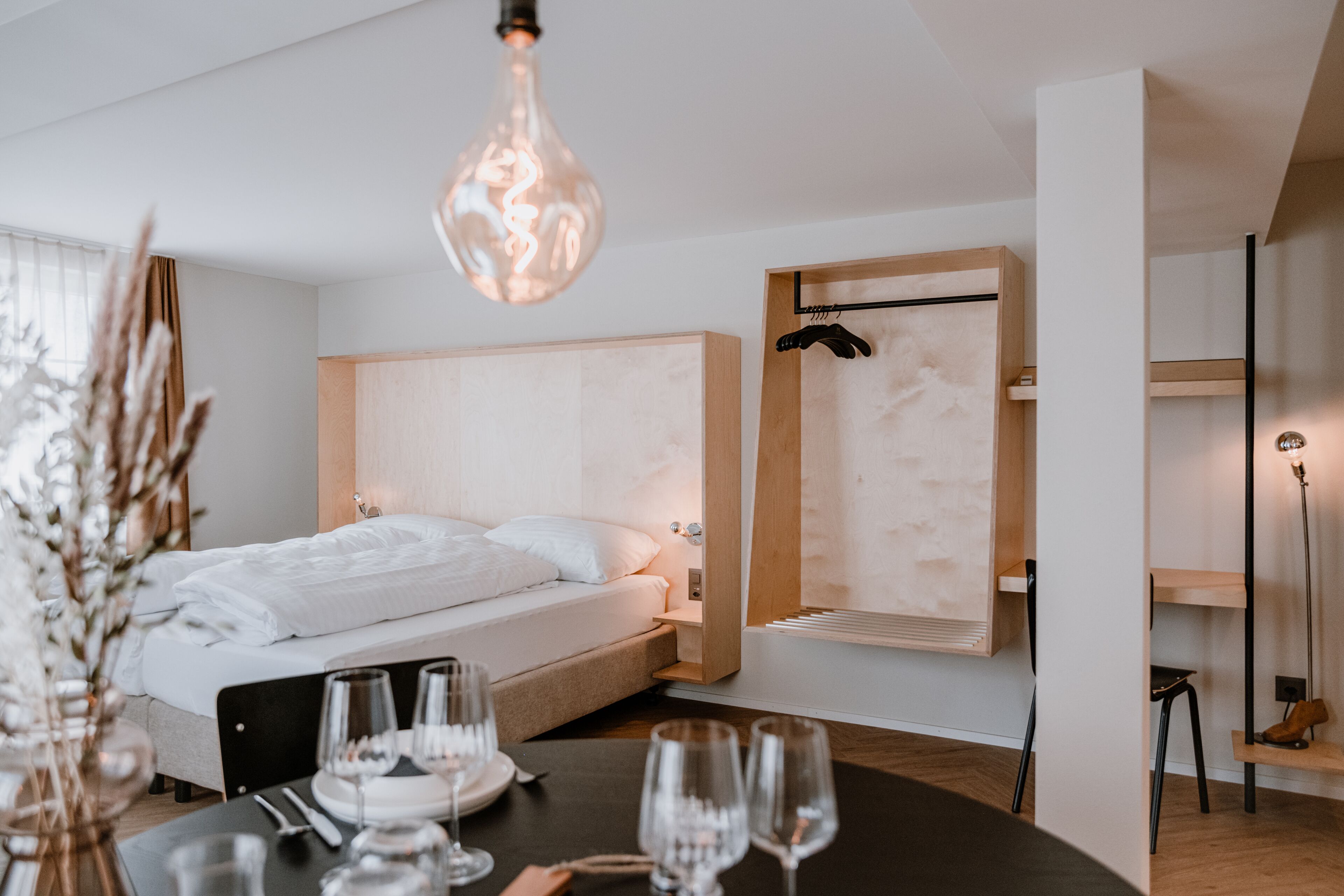 Quarto de hotel moderno com cama, mesa de cabeceira e luminária pendente.