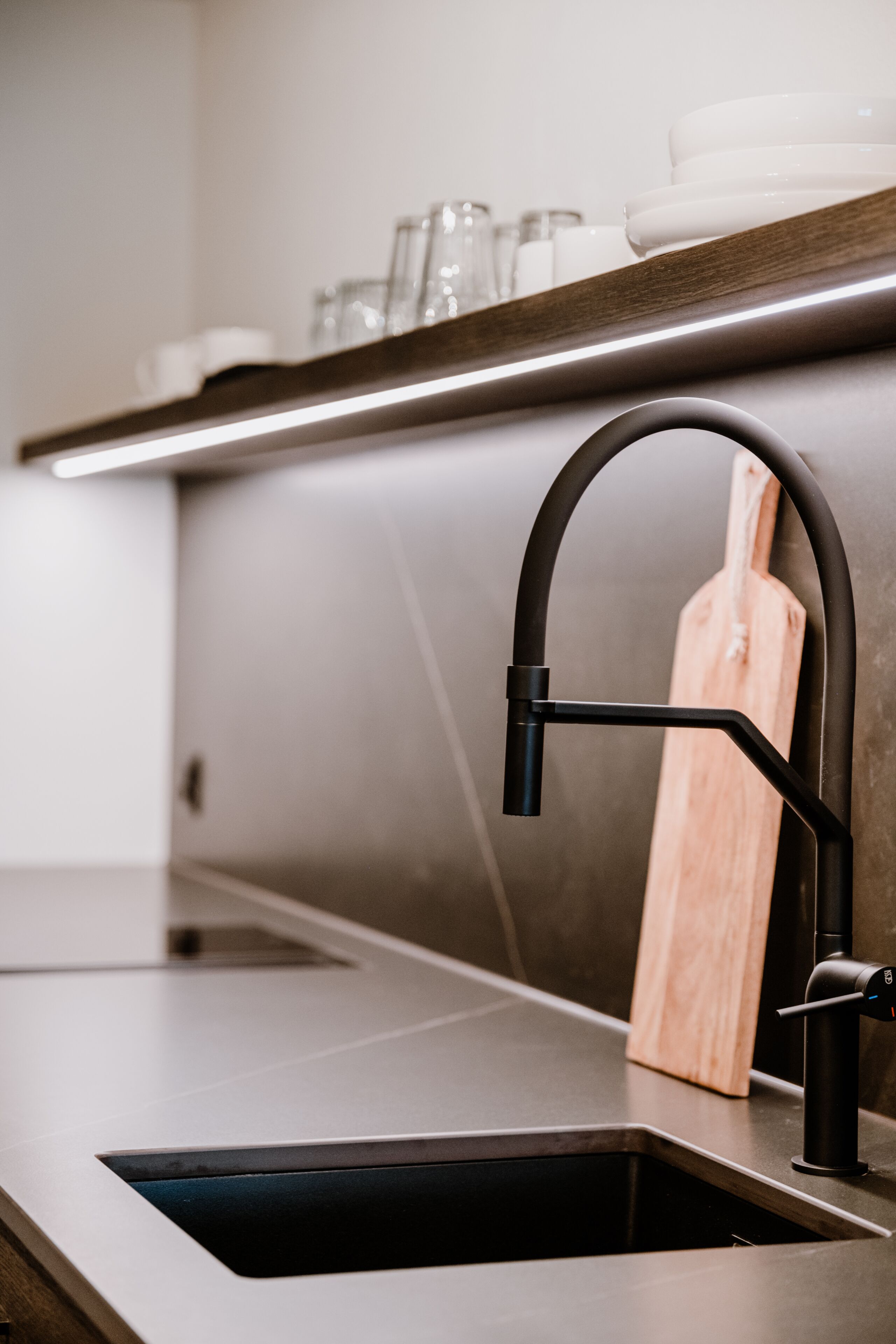 Una cocina moderna con un grifo negro elegante, una tabla de cortar de madera y un lavamanos de acero inoxidable.