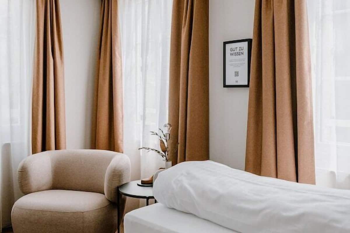 A hotel room with a bed, a round armchair, a small table, and a wall-mounted picture.