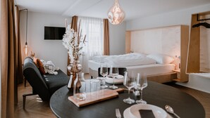 Una camera d'albergo moderna con un letto rifatto, un tavolo da pranzo apparecchiato per due e una televisione montata a parete.