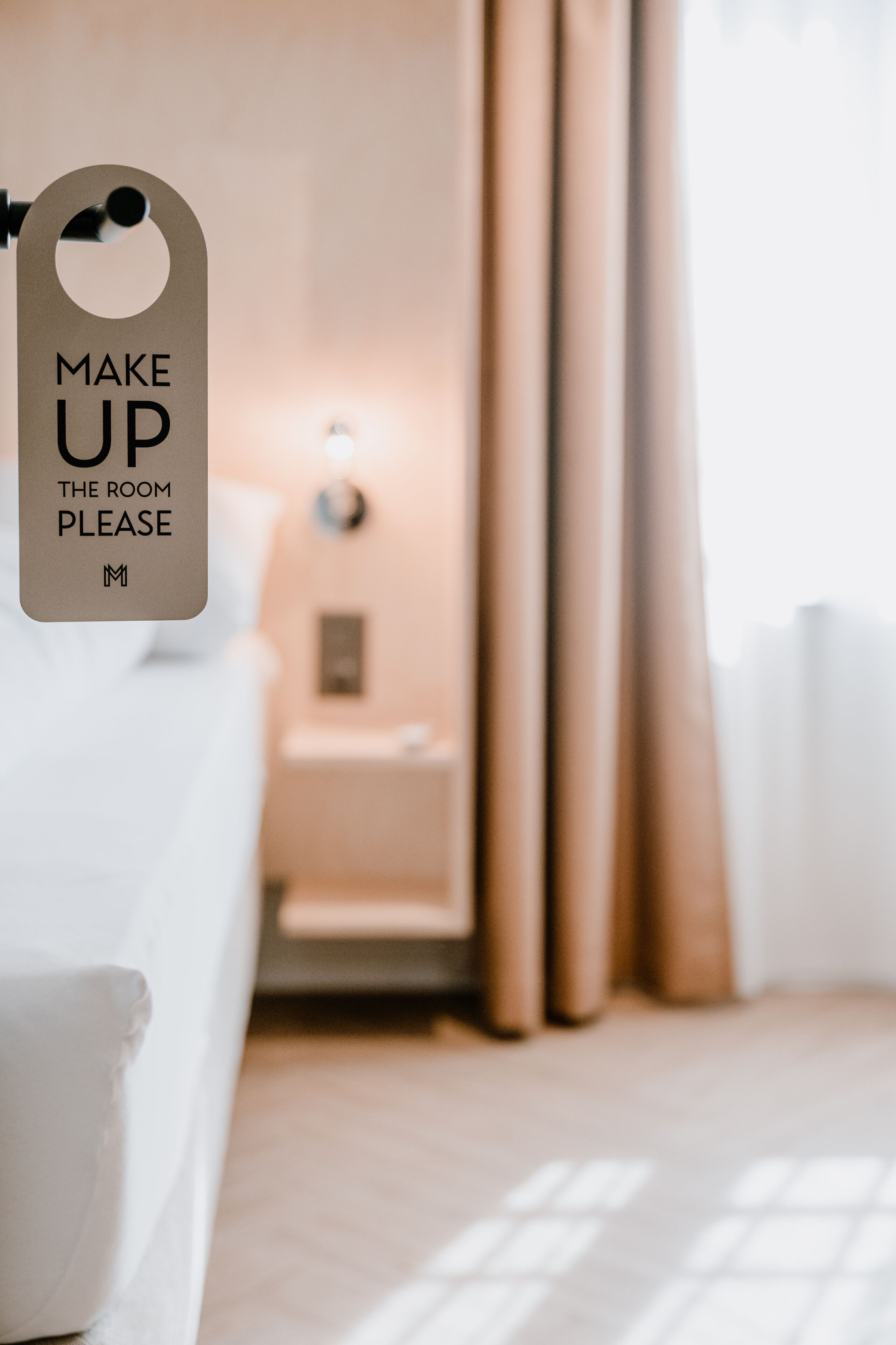 A hotel room with a bed, a nightstand, and a sign that reads "MAKE UP THE ROOM PLEASE".