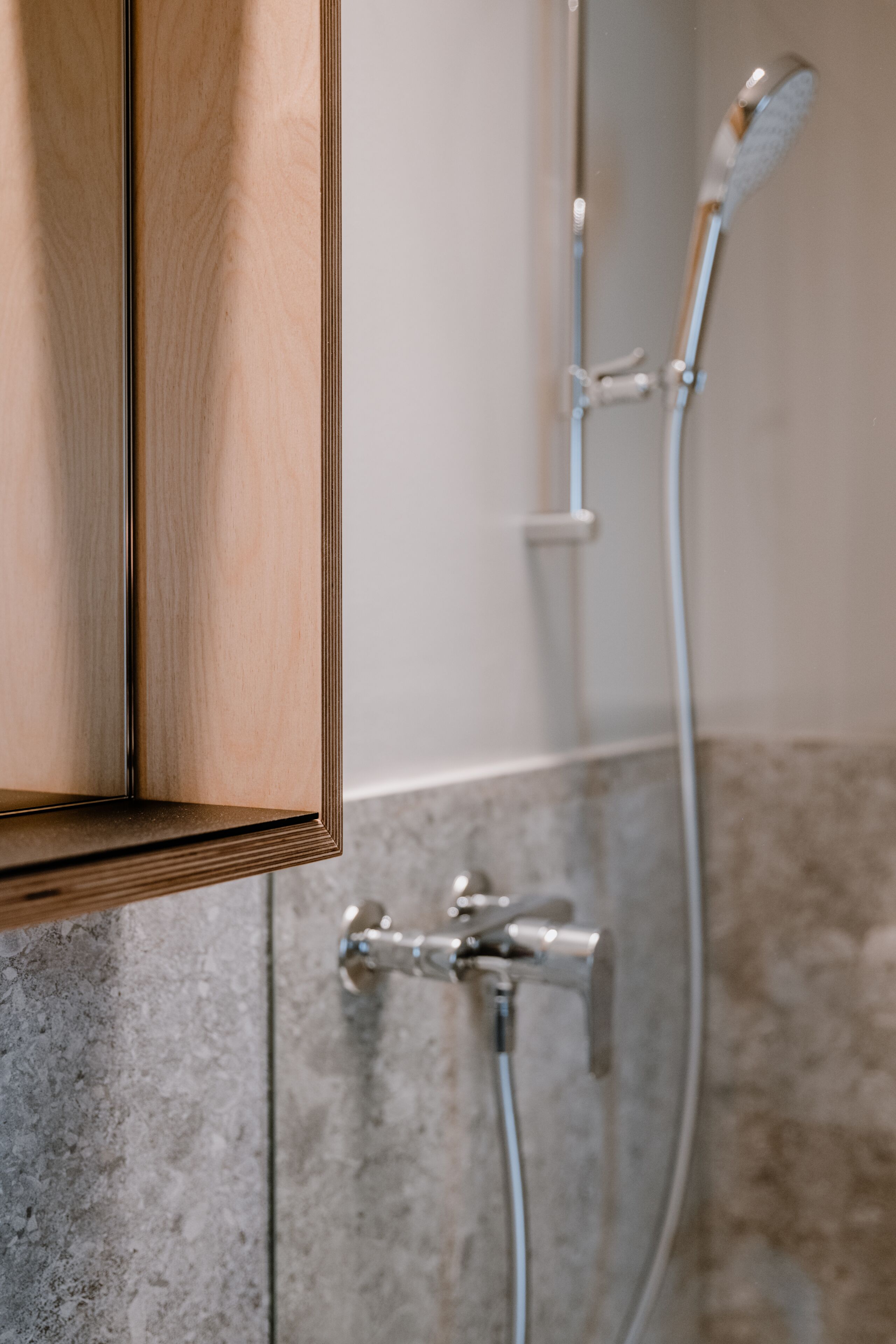 A bathroom with a wooden cabinet, a shower with a handheld showerhead, and a wall-mounted faucet.