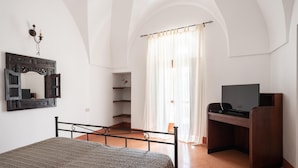Un dormitorio con cama, escritorio con televisor, espejo y ventana con cortinas.