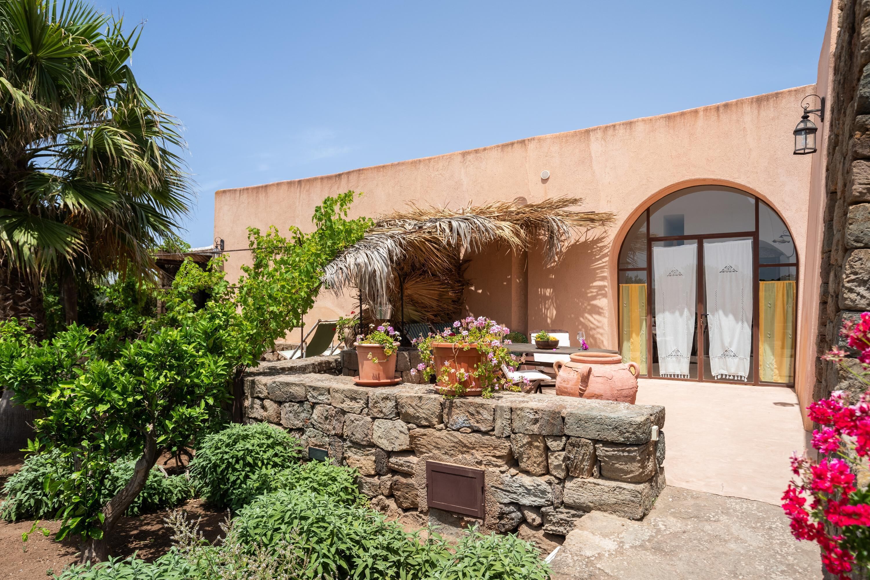 Un bâtiment avec un mur en pierre, des plantes en pot et un palmier.