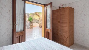 Een kamer met een bed, een houten garderobe en een open deur die leidt naar een buitenruimte met een stenen boog.