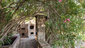 Un sentier de pierres mène à une construction rustique en pierre, dotée d’une petite entrée en arc de cercle.