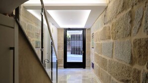 A hallway with stone walls, a glass railing, and a black door leading outside.