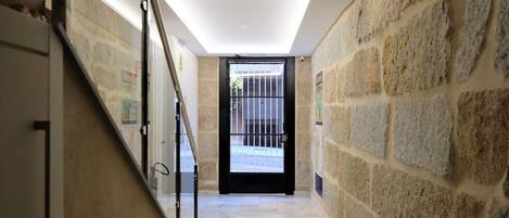 A hallway with stone walls, a glass railing, and a black door leading outside.
