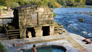 A stone building with a swimming pool, wooden deck, and a river in the background.