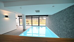 Una piscina interior moderna con vistas despejadas al exterior, una terraza de madera y una pared de ladrillo.