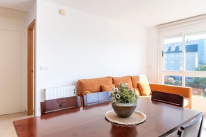 Un coin repas avec une table en bois, un arrangement floral en guise de décoration centrale et un canapé orange agrémenté de coussins.