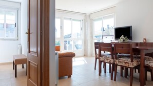 A bright room with a wooden door, a small bench, a sofa, a dining table with chairs, and a TV. - Apartment in Sanxenxo near Lapa Beach (Sanxenxo)