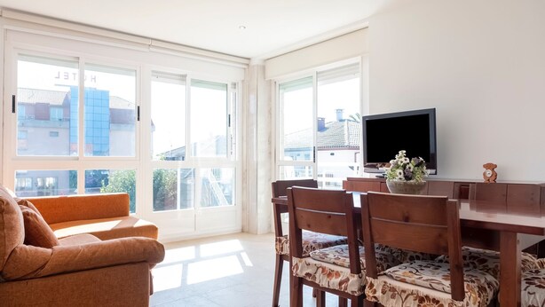 A bright room with a sofa, dining table, chairs, and a TV. - Apartment in Sanxenxo near Lapa Beach (Sanxenxo)