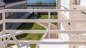 A balcony with white railings, a grassy area, and a paved path leading to a building with a stone facade. - Apartment in Sanxenxo near Lapa Beach (Sanxenxo)