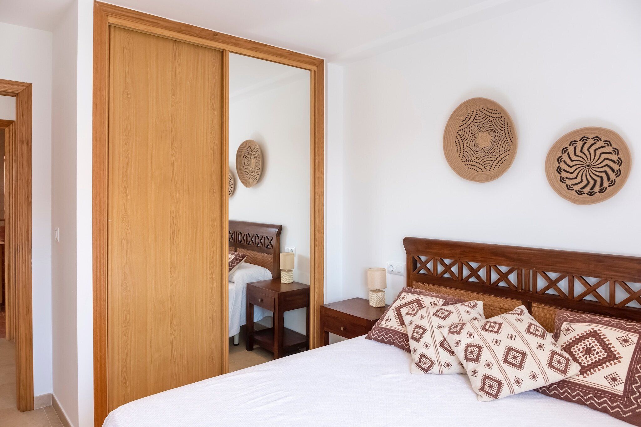 Un dormitorio con un armario de madera, una cama con almohadas estampadas y dos placas decorativas colgadas en la pared.