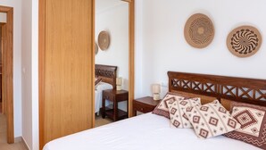 A bedroom with a wooden wardrobe, a bed with patterned pillows, and two wall-mounted decorative plates. - Apartment in Sanxenxo near Lapa Beach (Sanxenxo)