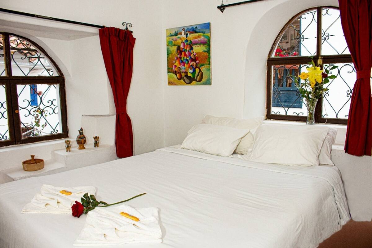 A bedroom with a bed, red curtains, a painting, and a vase with flowers.