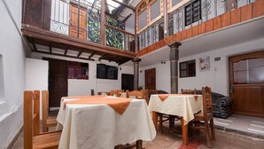 A dining area with tables set for four, wooden chairs, and a balcony with decorative iron railings. - Catama Inn Hotel (Cusco)