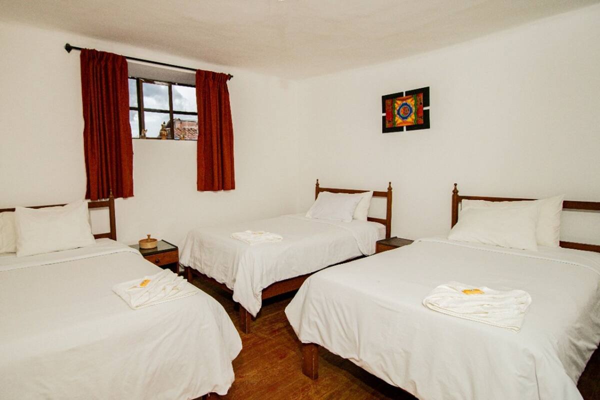 A room with two single beds, a window with red curtains, a small table, and a wall-mounted artwork.