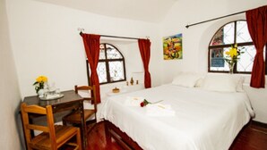 A bedroom with a bed, a desk with a chair, and two windows with curtains. - Catama Inn Hotel (Cusco)