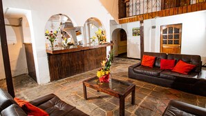 A lobby with a reception desk, a leather sofa with red cushions, a coffee table, and a stone floor. - Catama Inn Hotel (Cusco)