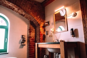 A bathroom with a brick wall, a wooden vanity, a mirror, a towel rack, and a window. - Elbe Resort Alte Ölmühle (Wittenberge)