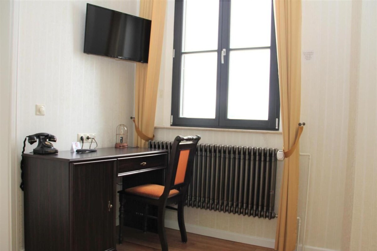 Una habitación con escritorio, silla, radiador y televisor montado en la pared.