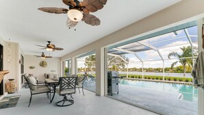 Amplia zona de patio con piscina, ventiladores de techo y una mesa de comedor con sillas.