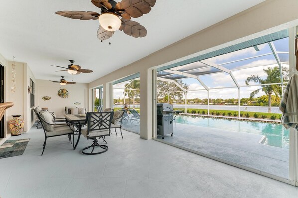 Un vaste patio doté d’une piscine, de ventilateurs de plafond et d’une table à manger avec des chaises.