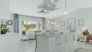 Una cocina moderna con armarios blancos, una isla central y una zona de comedor con un sofá y sillas blancos.