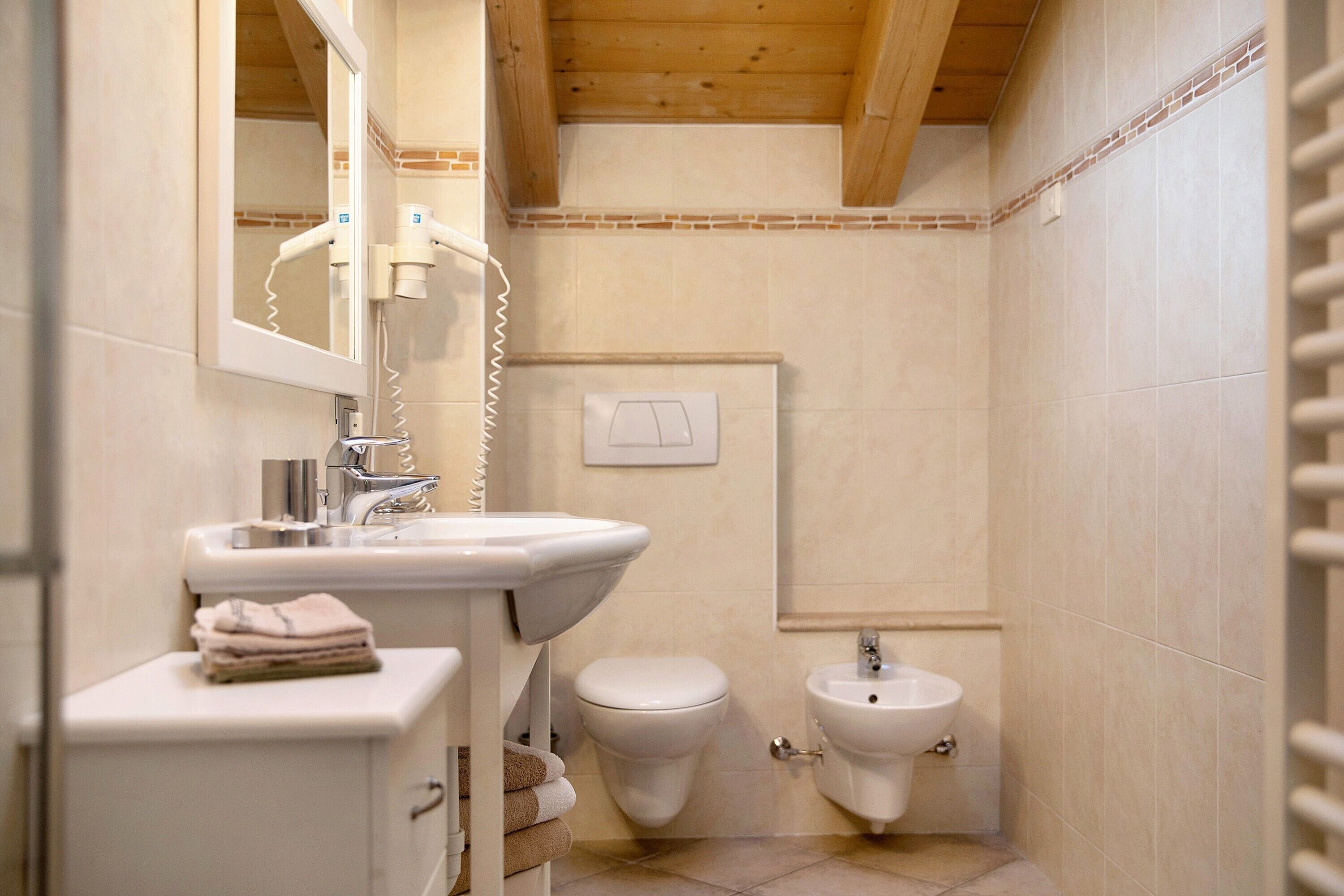 Een badkamer met een wastafel, toilet, bidet en een stapel handdoeken.