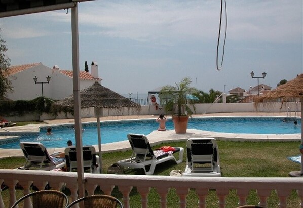 A pool area with lounge chairs, a thatched roof structure, and a view of the sea.