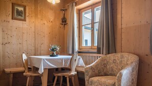 A wooden dining area with a table, chairs, and a floral-patterned armchair. - Holiday Apartment 'Haus Thurn Apartment A' with Mountain View, Garden & Wi-Fi (Kastelruth)