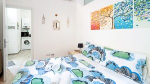 Ein Schlafzimmer mit einem Bett, einem Nachttisch, einer Wand-Klimaanlage, einer Waschmaschine und einer Tür zu einem anderen Raum.