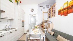 Eine moderne Küche mit weißen Schränken, einem Esstisch für vier Personen und einem grauen Sofa mit Kissen.