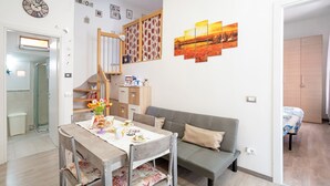 Ein Essbereich mit einem Holztisch, Stühlen und einer Couch. Eine Treppe mit Holzbalken, eine Wanduhr und ein Gemälde sind ebenfalls zu sehen.