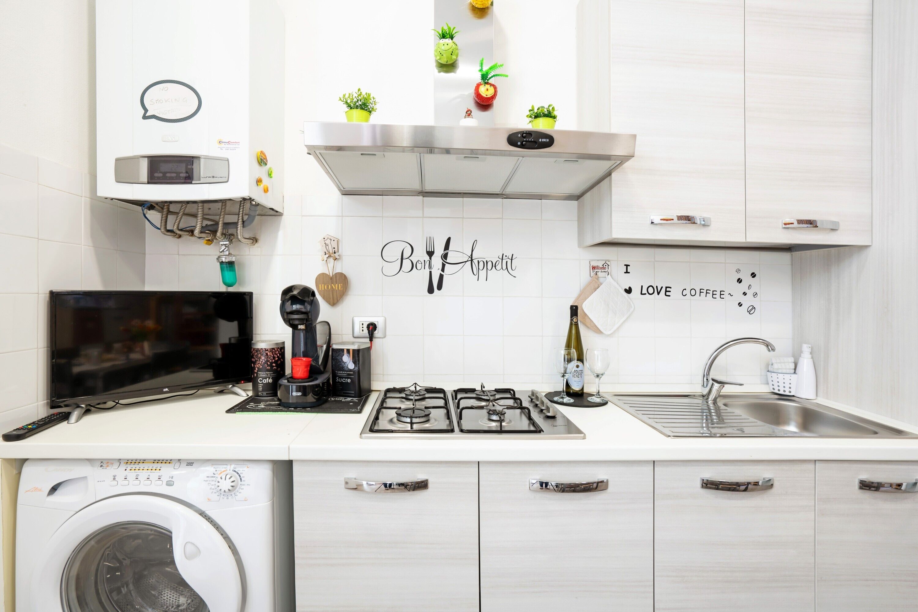 Une cuisine moderne équipée d’un lave-linge, d’une machine à café et d’un verre à vin posé sur le plan de travail.