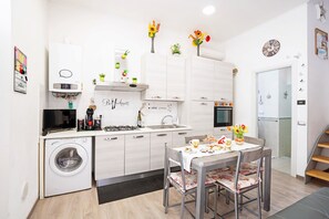 Cocina compacta con lavadora, mesa de comedor con sillas, microondas, lavaplatos y armarios.