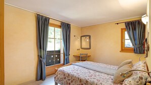 A bedroom with a bed, a chair, a desk, and a window with curtains.