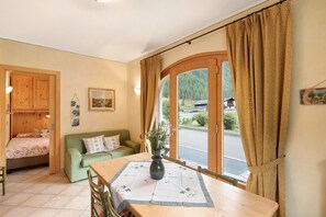 A cozy room with a bed, a green sofa, a dining table with a vase, and a large window with curtains.