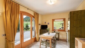 A room with a dining table, chairs, a television, and a window with curtains.