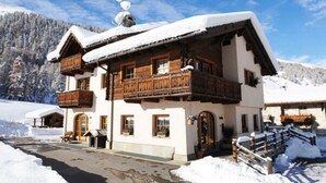 A wooden chalet with a balcony, snow-covered roof, and a mountain backdrop.