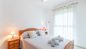A neatly made bed with pillows, a bedside lamp, and rolled towels. - Pet-Friendly Apartment 'Edificio Menorca' close to the Sea with Shared Pool & Wi-Fi (Alicante)