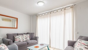 A living room with a sofa, a small table, and a window with curtains. - Pet-Friendly Apartment 'Edificio Menorca' close to the Sea with Shared Pool & Wi-Fi (Alicante)