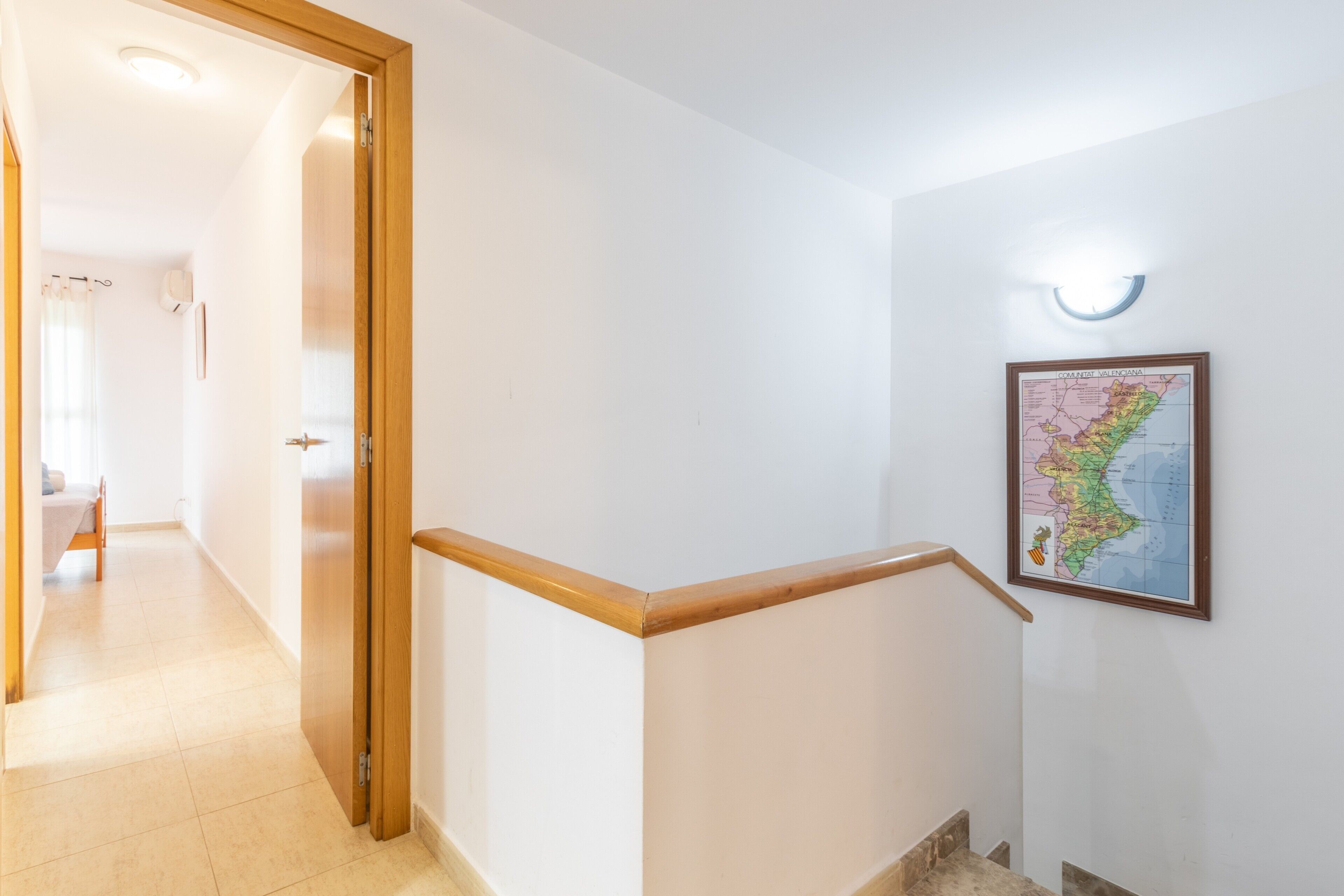 Un pasillo con una puerta de madera, una escalera con barandilla y un mapa colgado en la pared.