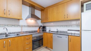 A kitchen with wooden cabinets, a stainless steel sink, a built-in oven, a dishwasher, and a microwave. - Pet-Friendly Apartment 'Edificio Menorca' close to the Sea with Shared Pool & Wi-Fi (Alicante)